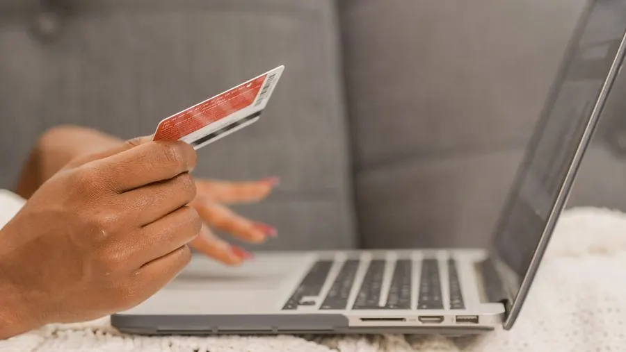 Shopper holding a credit card while completing an online checkout on a laptop
