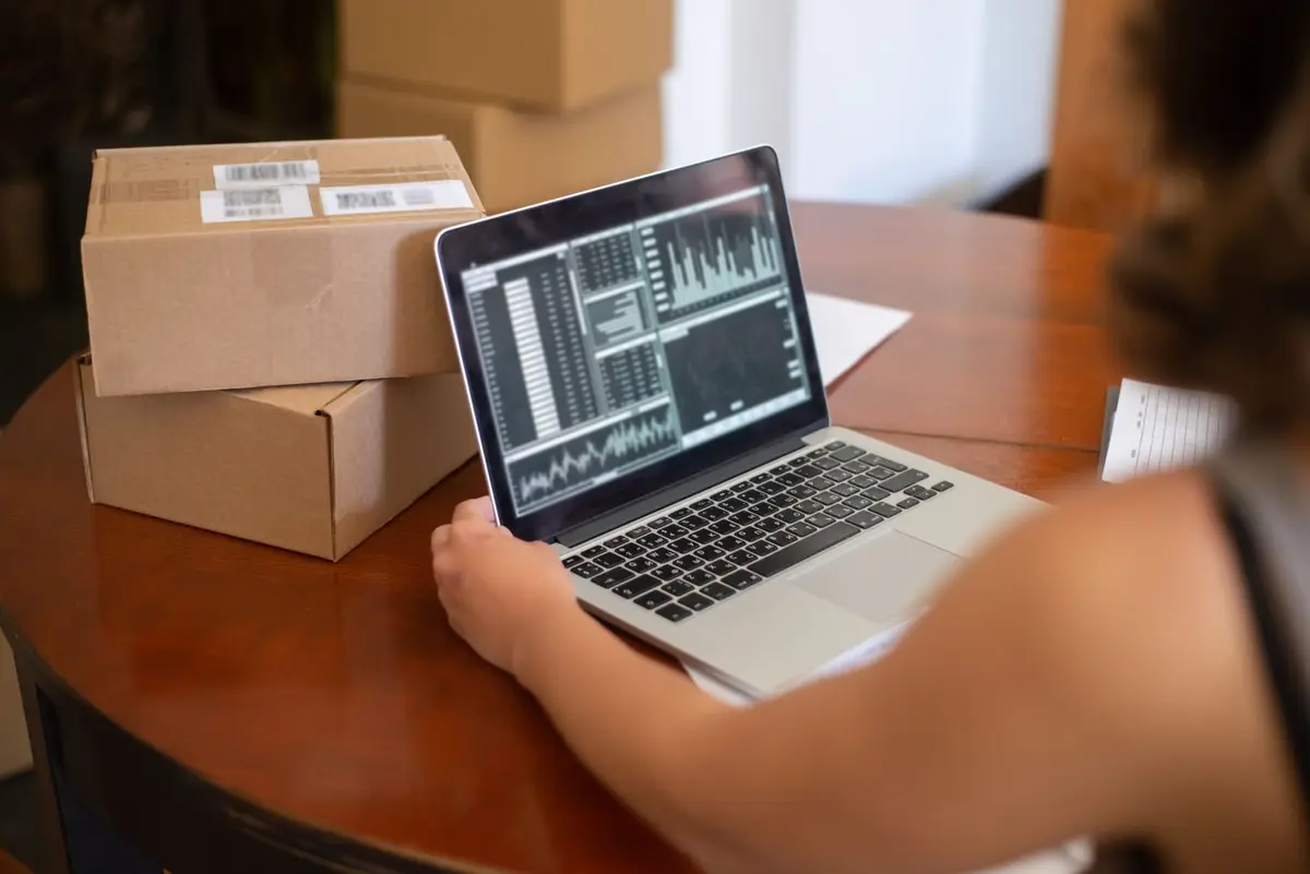 Online store owner reviewing store analytics on a laptop beside packed parcels