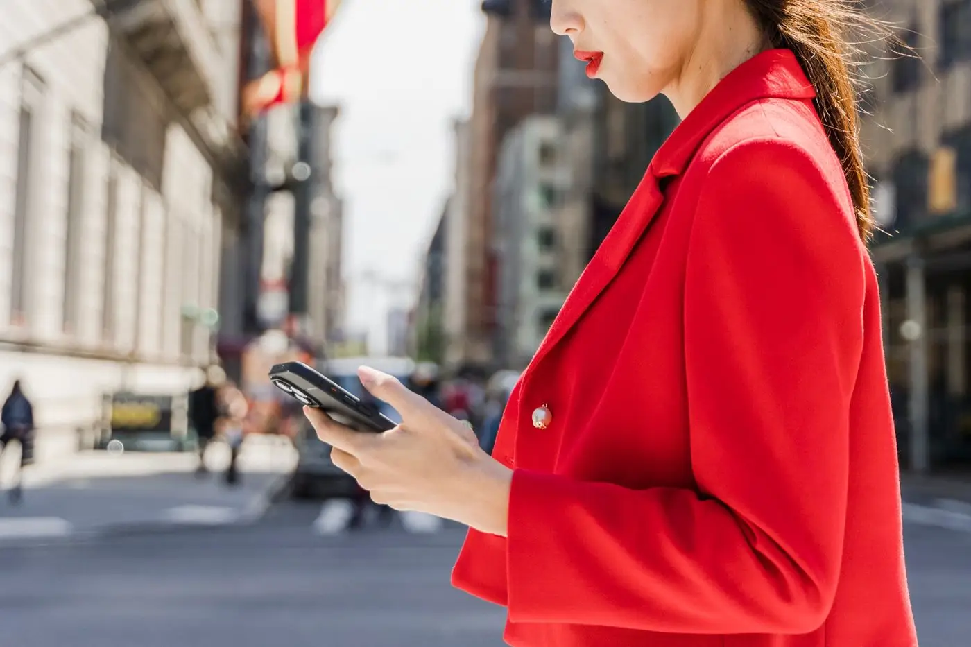 A woman in a red blazer stops on a city pavement to check her phone mid-street — the moment a local seo singapore search happens.