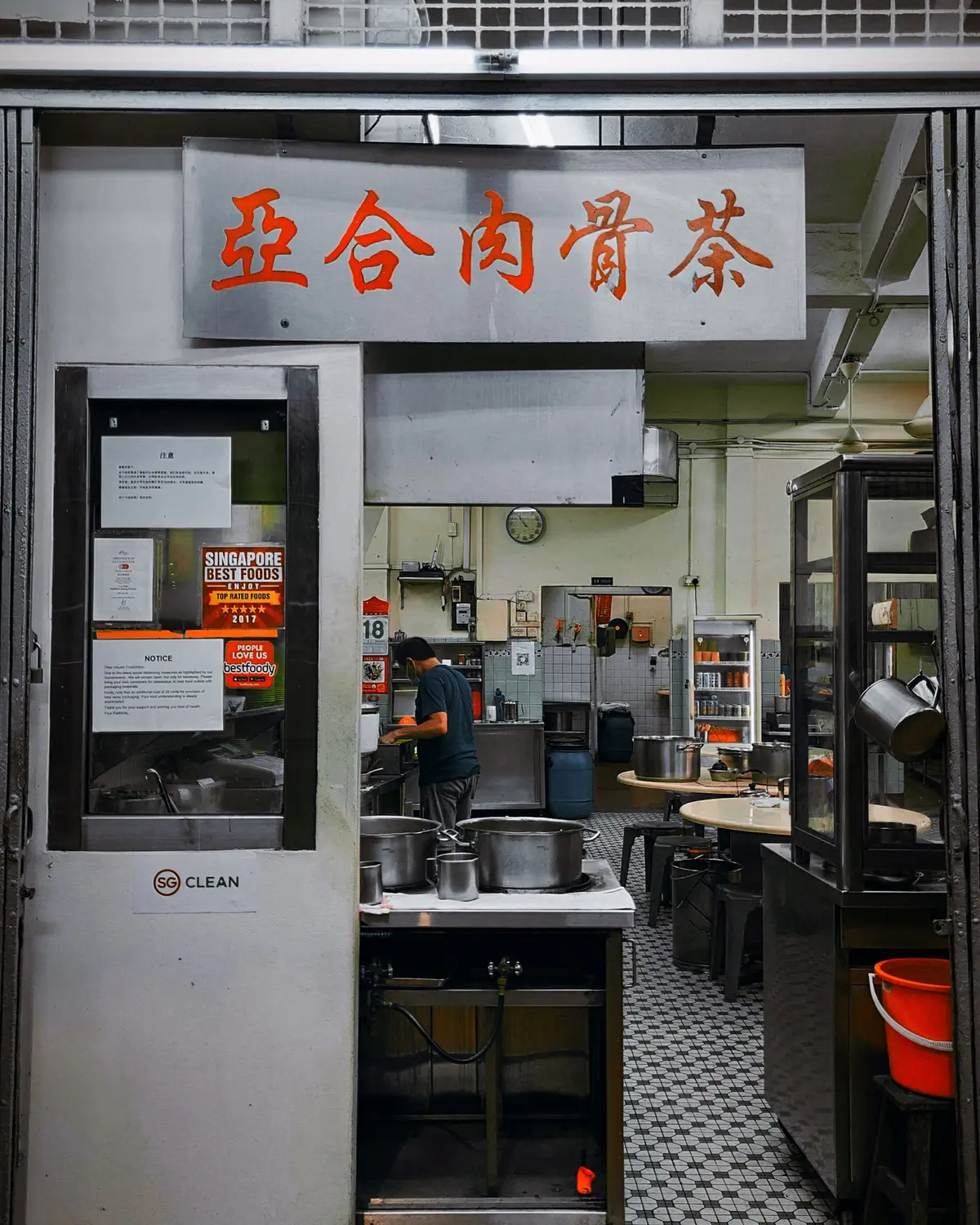 A Singapore bak kut teh shop with its red painted signboard, an SG CLEAN decal on the door and a cook working at the stockpots — the business name on the signage is where google business profile optimisation singapore starts.