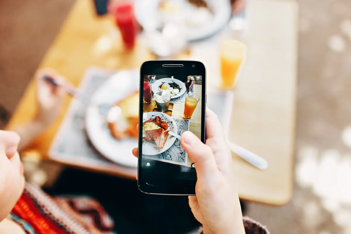 Two hands hold a phone in front of a brunch table, the live camera view filling the screen — the kind of photograph a profile is supposed to carry.