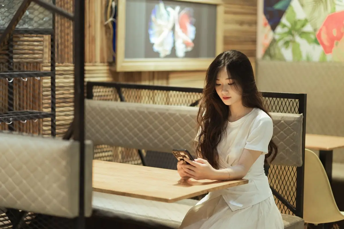 A young woman sits alone in a rattan-panelled restaurant booth looking at her phone — where a genuine review actually gets written, and part of what local search ranking singapore is built on.