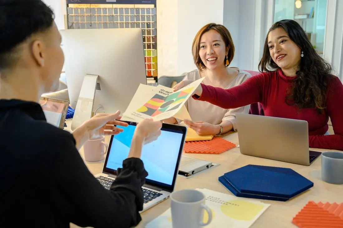 Colleagues handing over a printed report across a desk in an office
